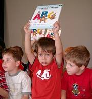 Ein Hoch auf das ABC! Zwischen zwei Kindern streckt ein Junge ein Buch mit der Aufschrift "ABC" in die Höhe.